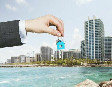 A hand is holding a key from the new home. A concept of real estate property agency. Miami cityscape on the background.
